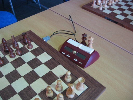 Electronic chess board connected to a digital chess clock with pieces arranged for play